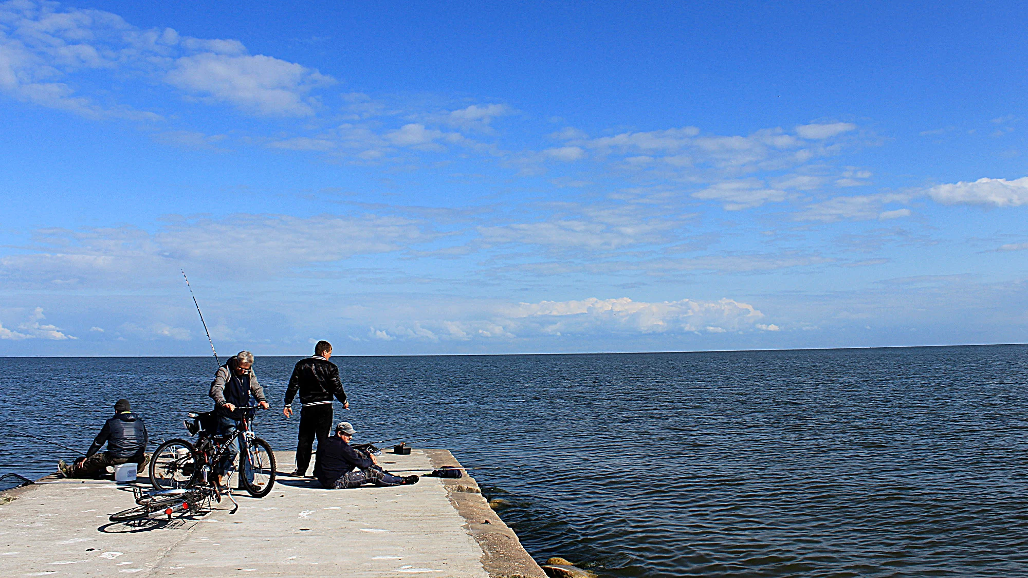 Four fishermen at the end of a dock by the Baltic Sea with blue sky in Lithuaia.