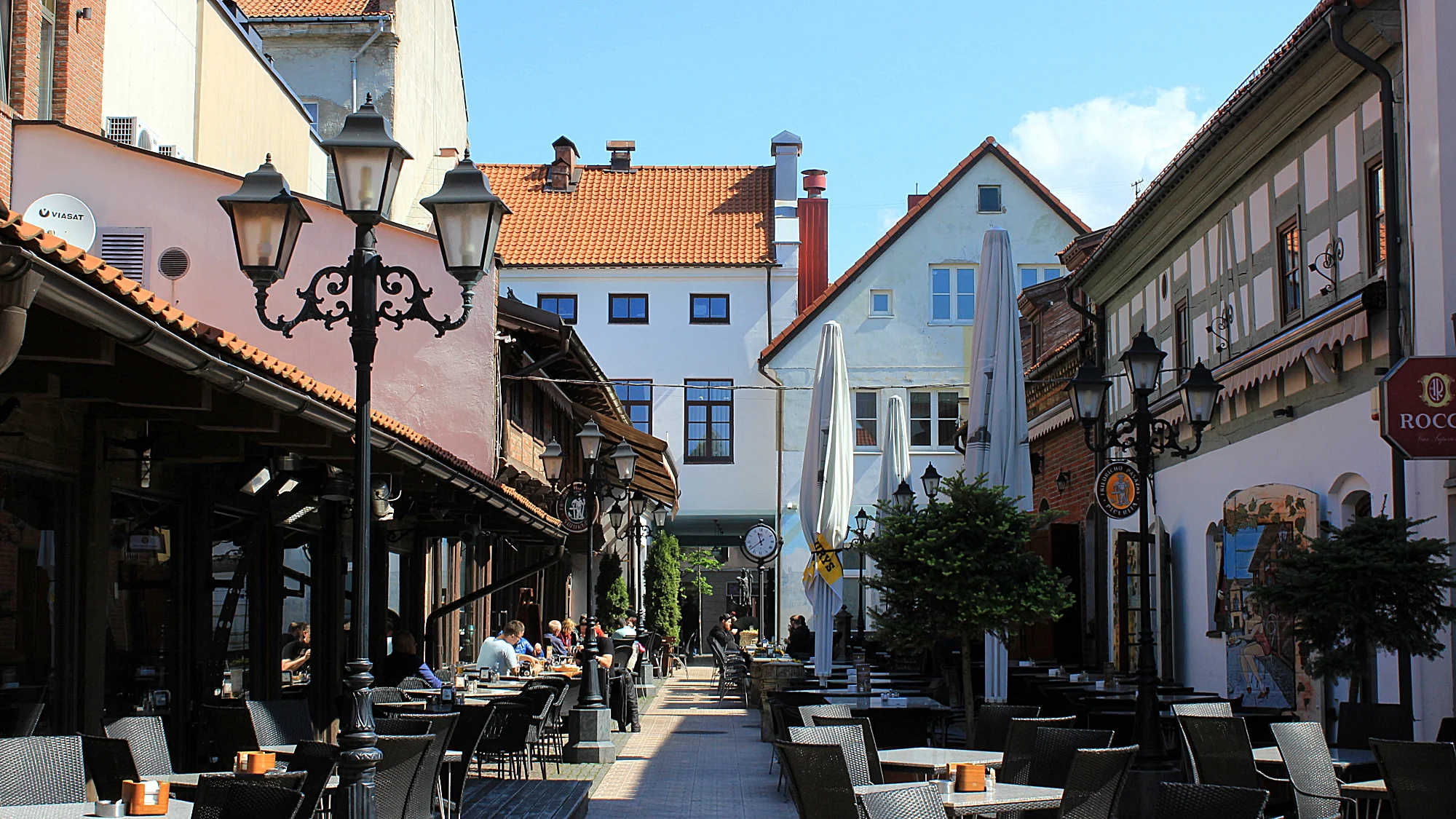 An empty, narrow sidestreet at the Old Town of Klaipeda with beautiful old buildings, an old lamp post and empty cafeteria tables.