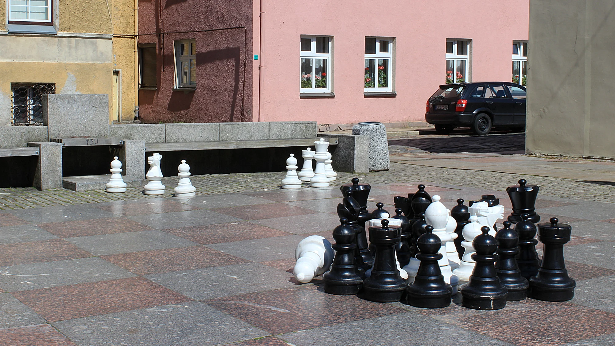 A giant public chessboard made of marble with most chess pieces collected in one cluster in Klaipeda.