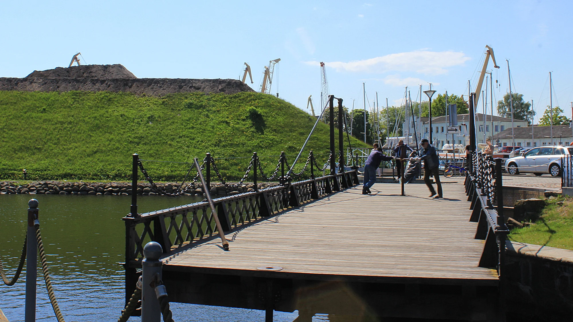 Two men mechanically rotating a bridge in Klaipeda with the Klaipeda Fort in the background.