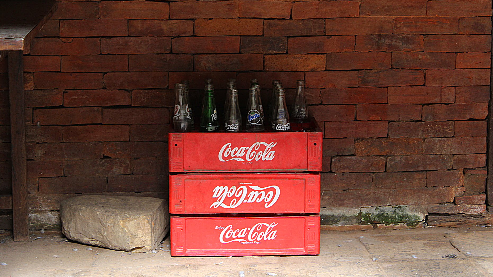 Coca-Cola containers and empty glass bottles in Durbar Square of Kathmandu by a brick wall.