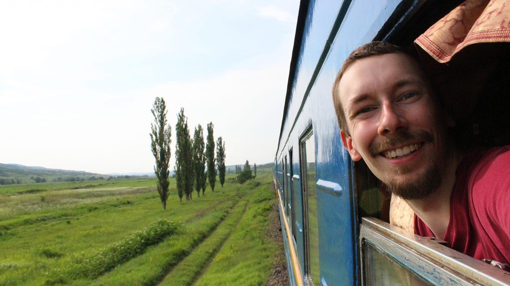 How to waste time during long train journeys? A tourist taking a selfie peeking from an open train window.