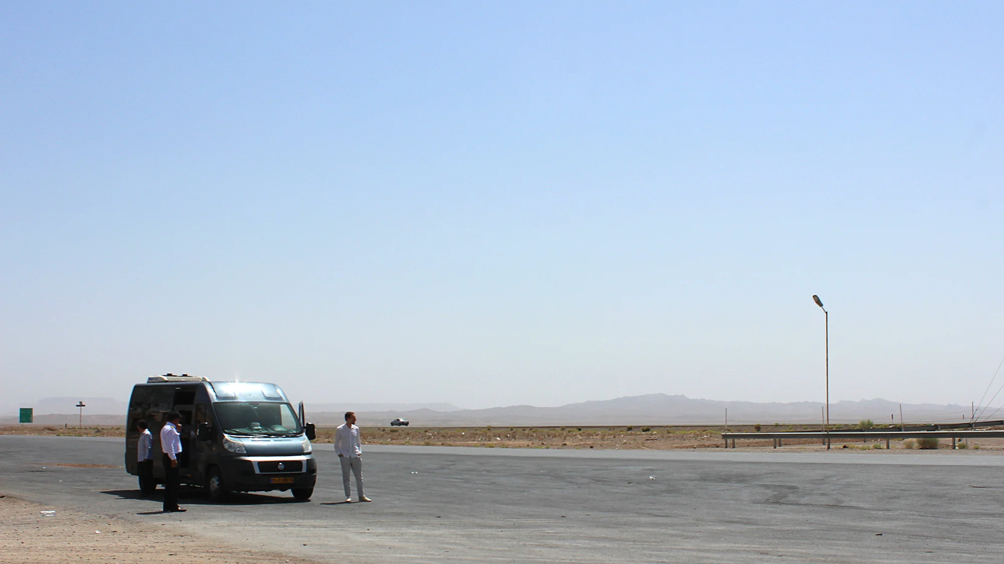 A grey minibus at the side of the road on a desert during a guided tour of Iran.