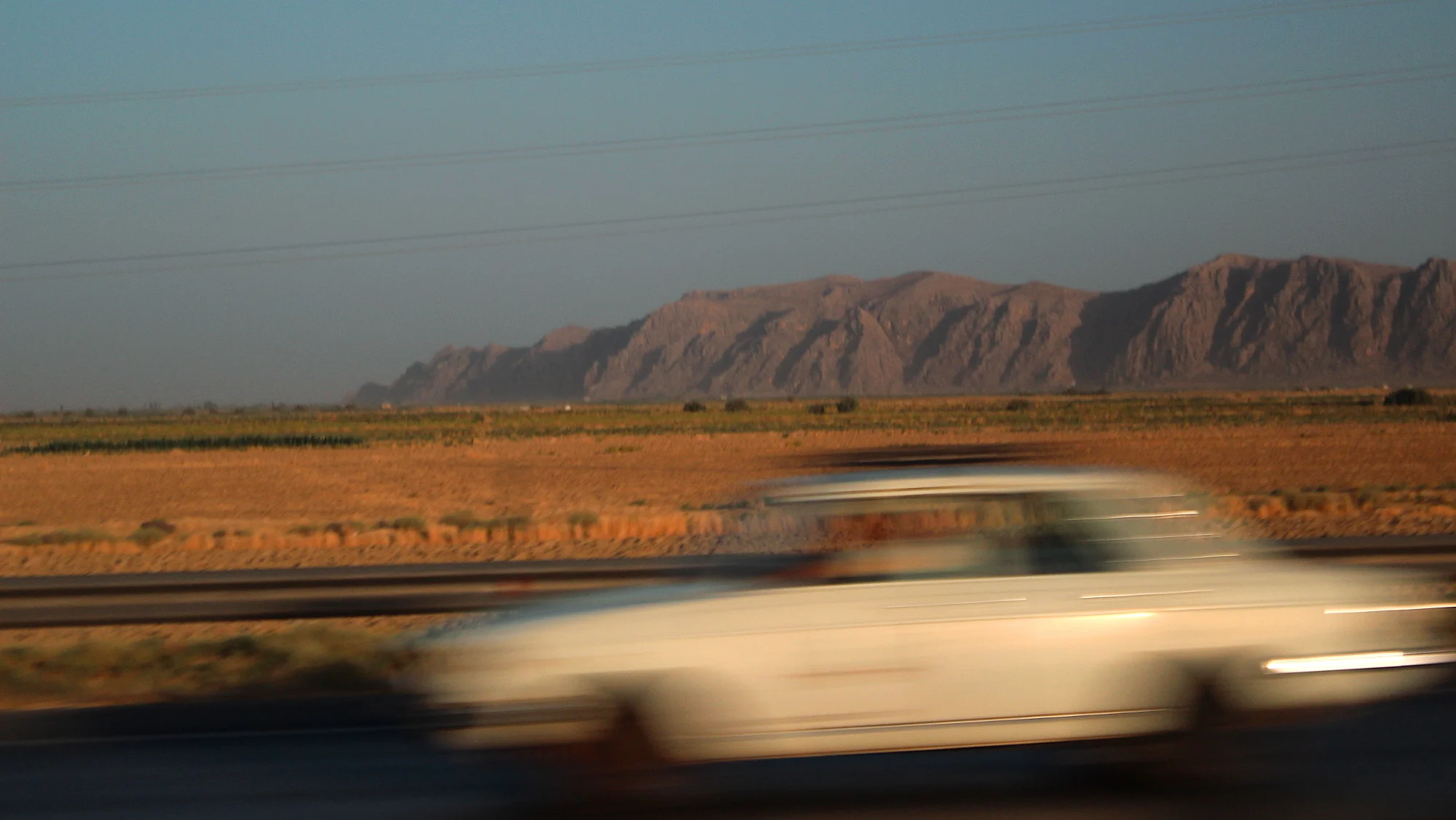 Guided tour of Iran. An atmospheric travel picture of a car driving past with sunset, desert and mountains.