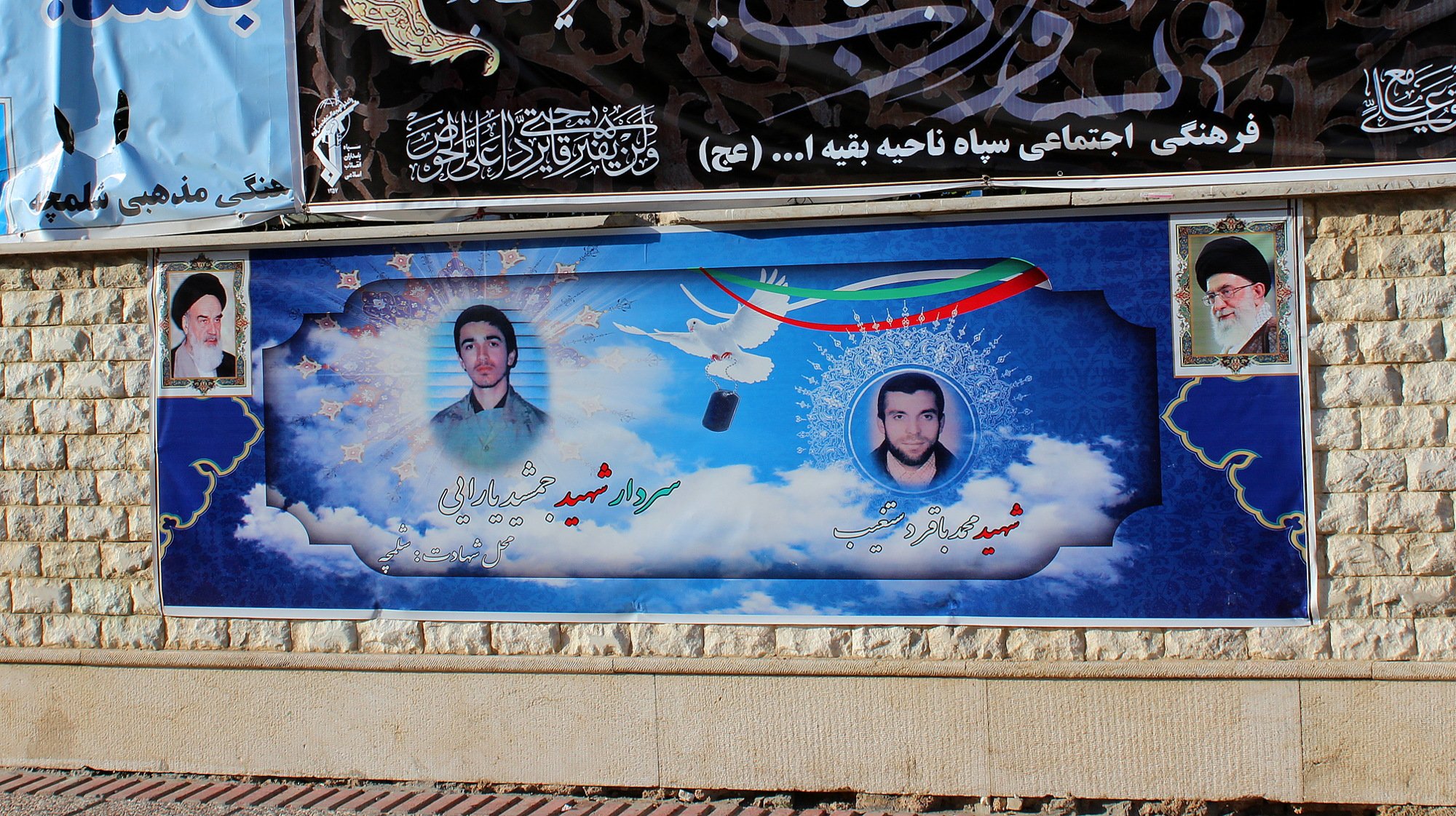 A poster of the Supreme Leaders of Iran and two assassinated nuclear scientists on the wall of a building.