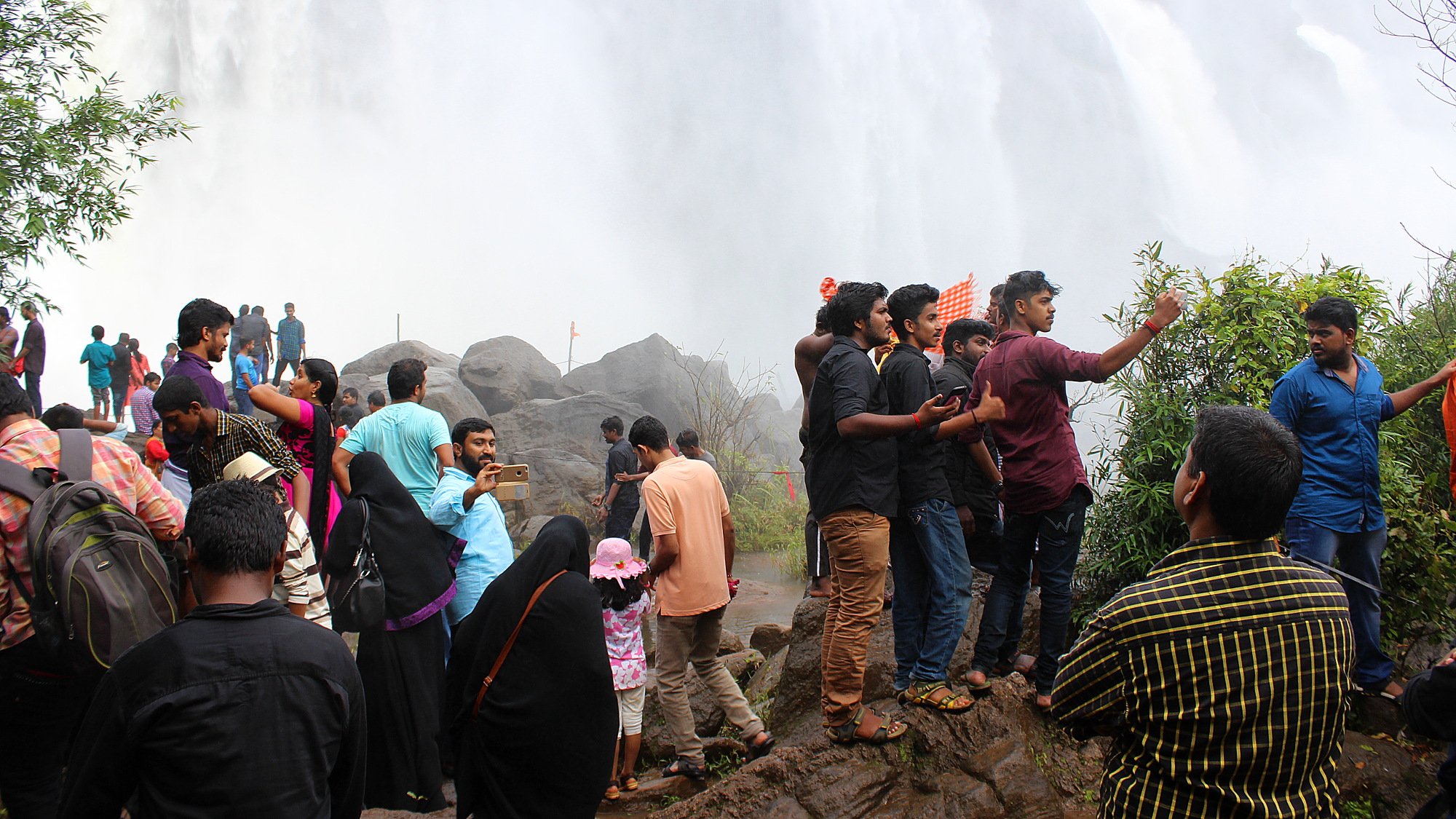 Indian tourists taking selfies below the Athirappilly Falls waterfall.