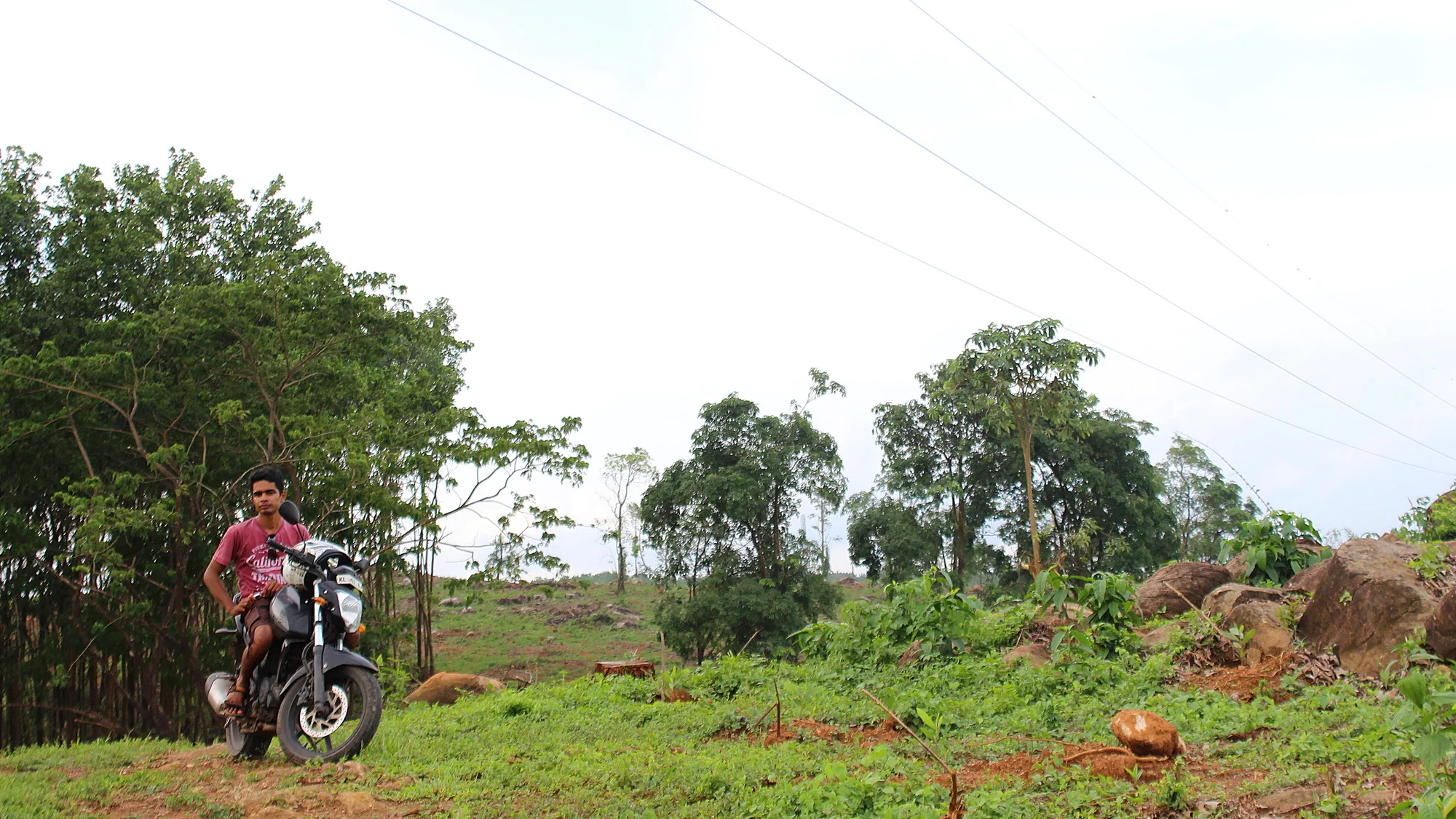 Monsoon travel in Kerala. A young man from Kerala posing in a green hill with a motorcycle.