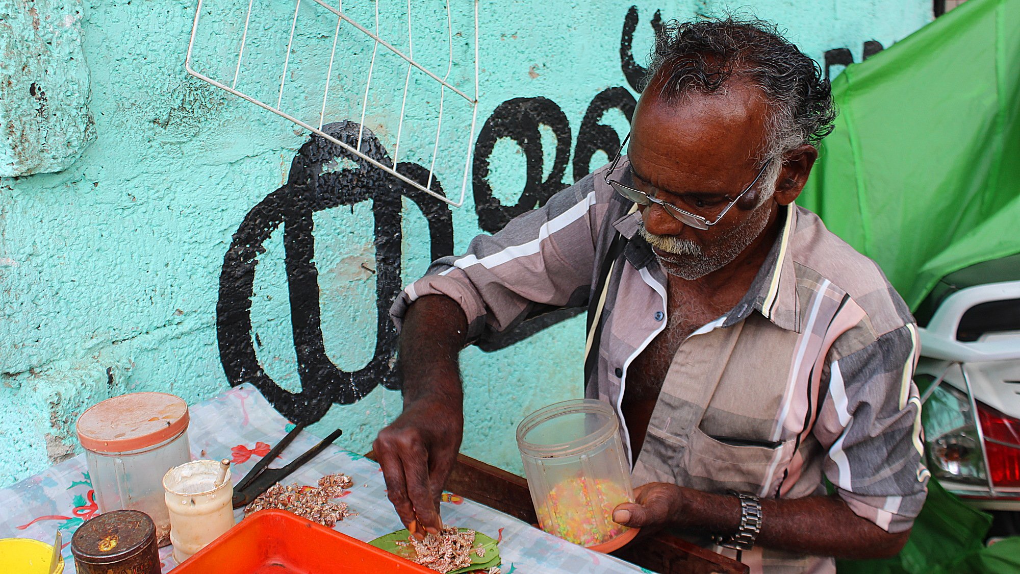 Street vendor making chewable tobacco paan from different ingredients including sprinkles in India.