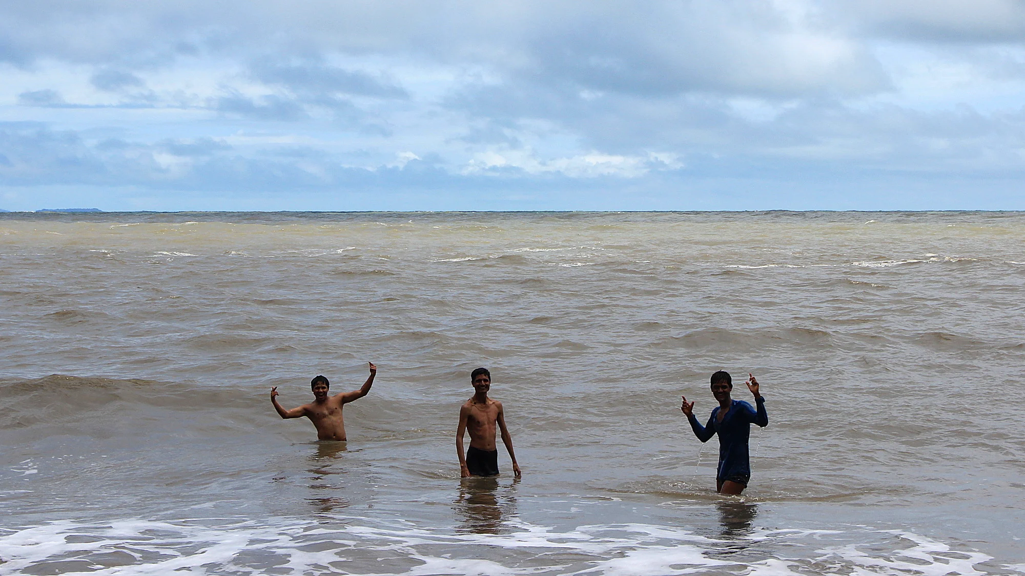 Three young Indian men swimming at Om Beach and posing for the camera.