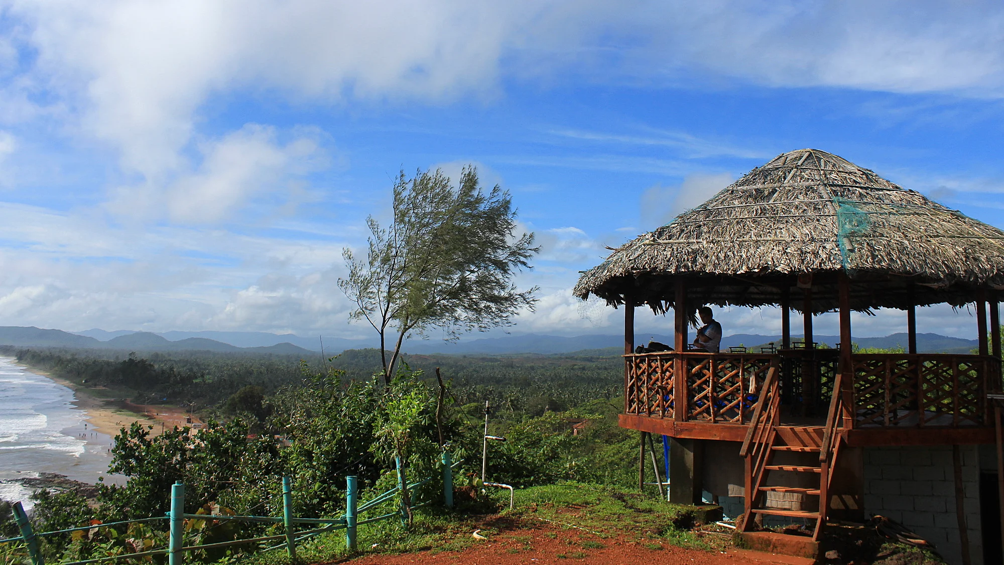 The yard of Zostel Gokarna with blue sky and a viewpoint restaurant hut on the hill.