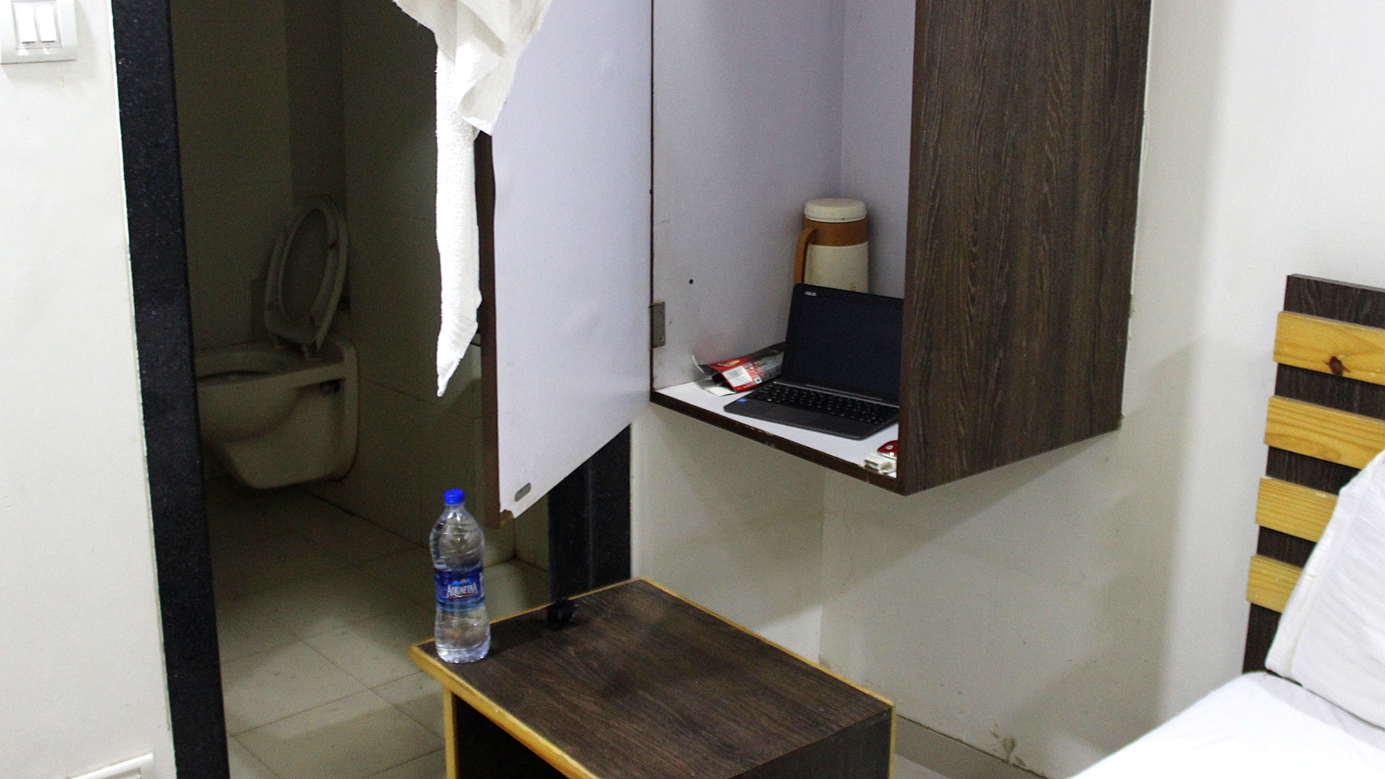 An improvised desk with laptop on a locker and hotel room nightstand used as a chair.
