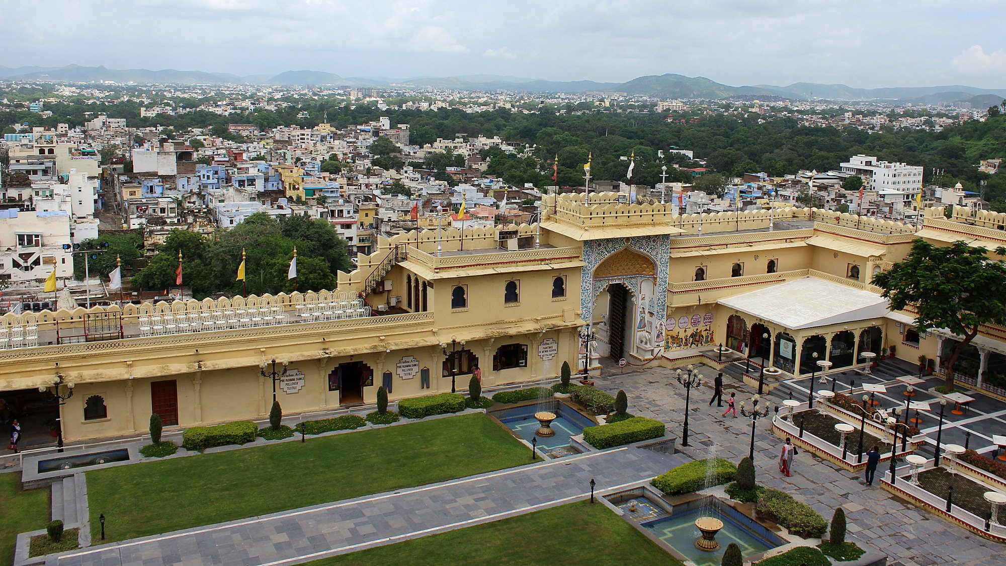 The courtyard of the City Palace of Udaipur from above with a high yellow wall between the yard and the city.