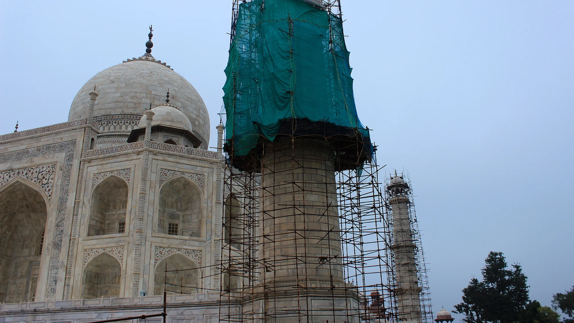 Partly covered minaret tower in front of Taj Mahal under renovation.