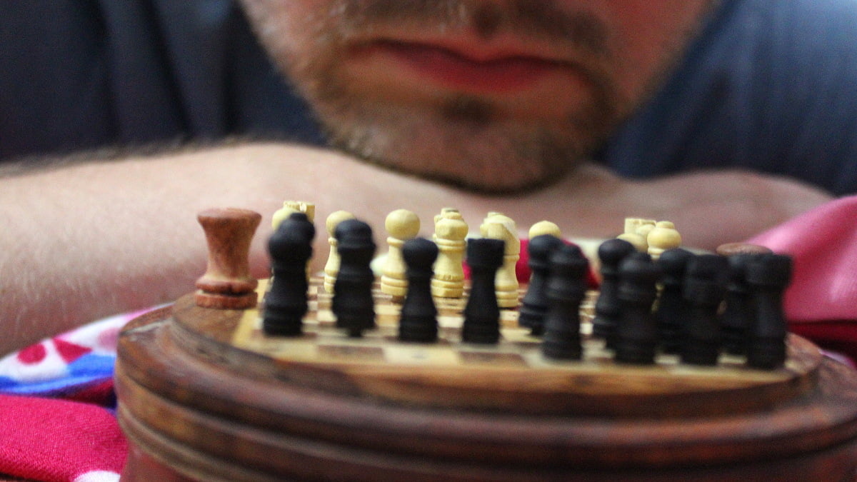 Playing chess with a travel companion in India. A miniature chess board carved of wood and a player in the background.