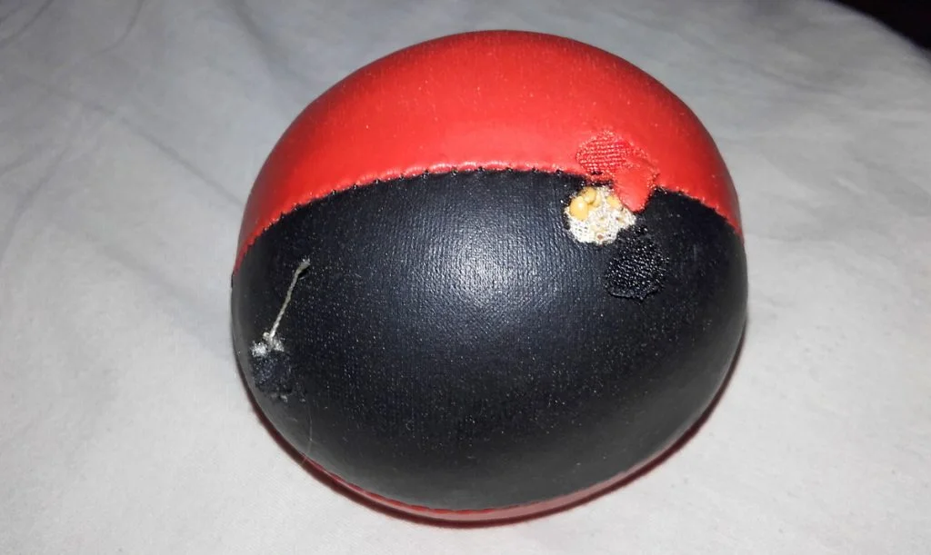 A striped red and black juggling ball with a hole in it and seeds inside.
