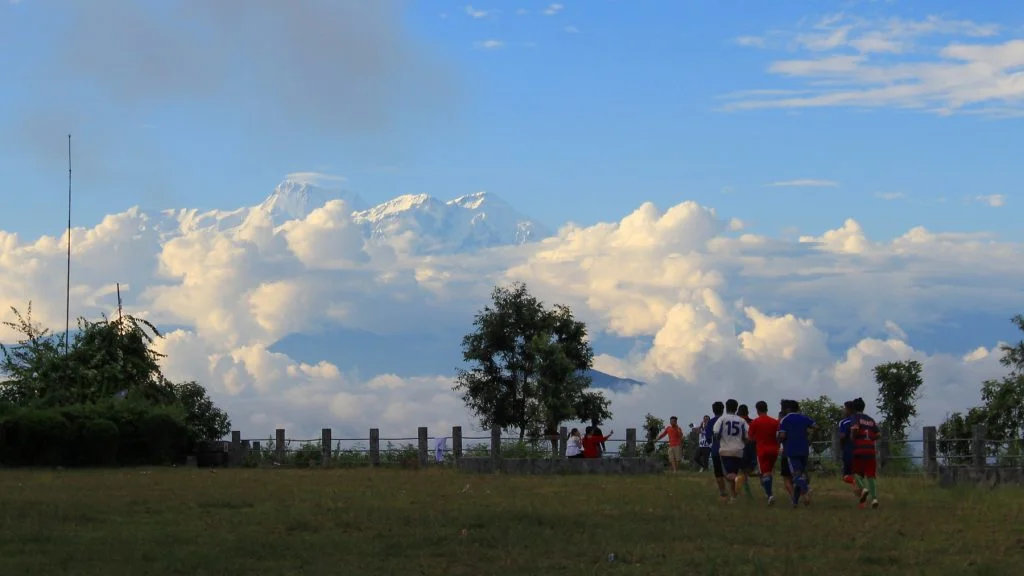Where to see Himalayas in Nepal. Children playing football in Tundikhel, Bandipur, Nepal with high Himalayan mountain rising in the background.