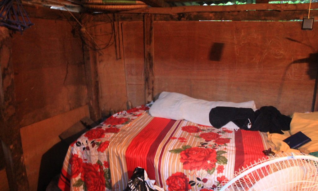 A room in a Nepalese shack with a small bed and walls made of chipboard.