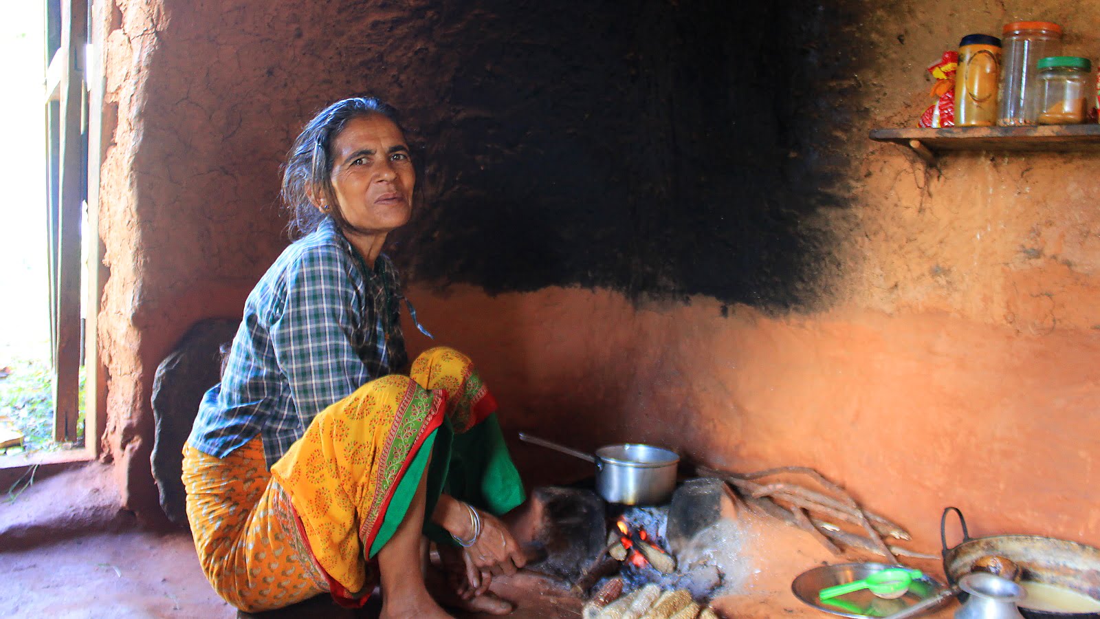 A Nepalese woman cooking food in a traditional ground stove.