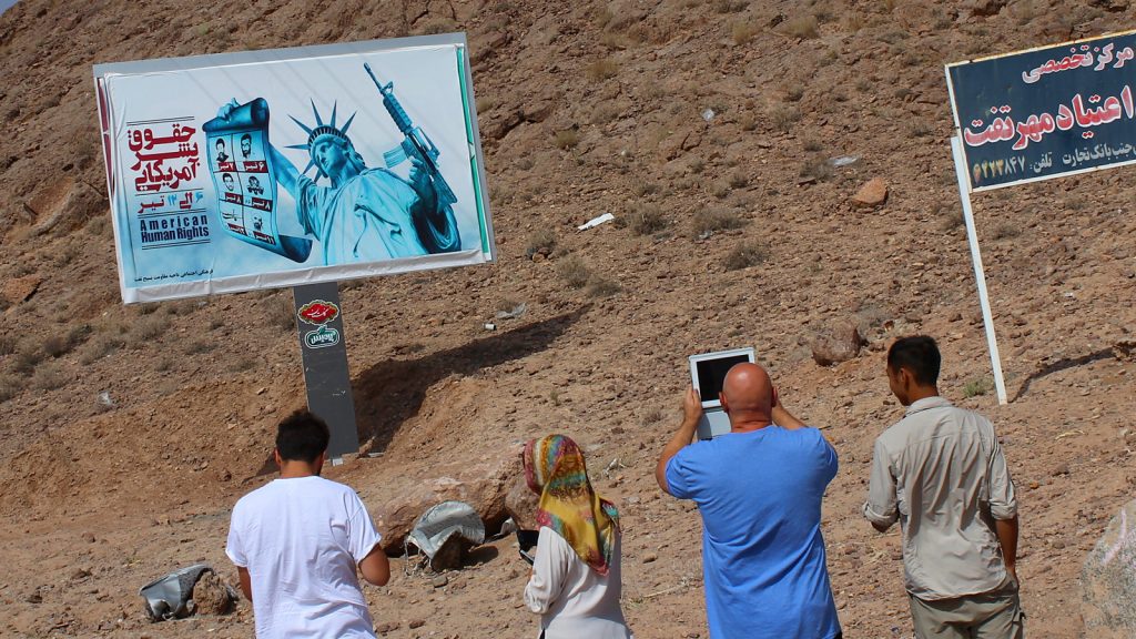 Things you miss when you travel. Tourists taking a photograph of an anti-American propaganda billboard by the side othe road in Iran.