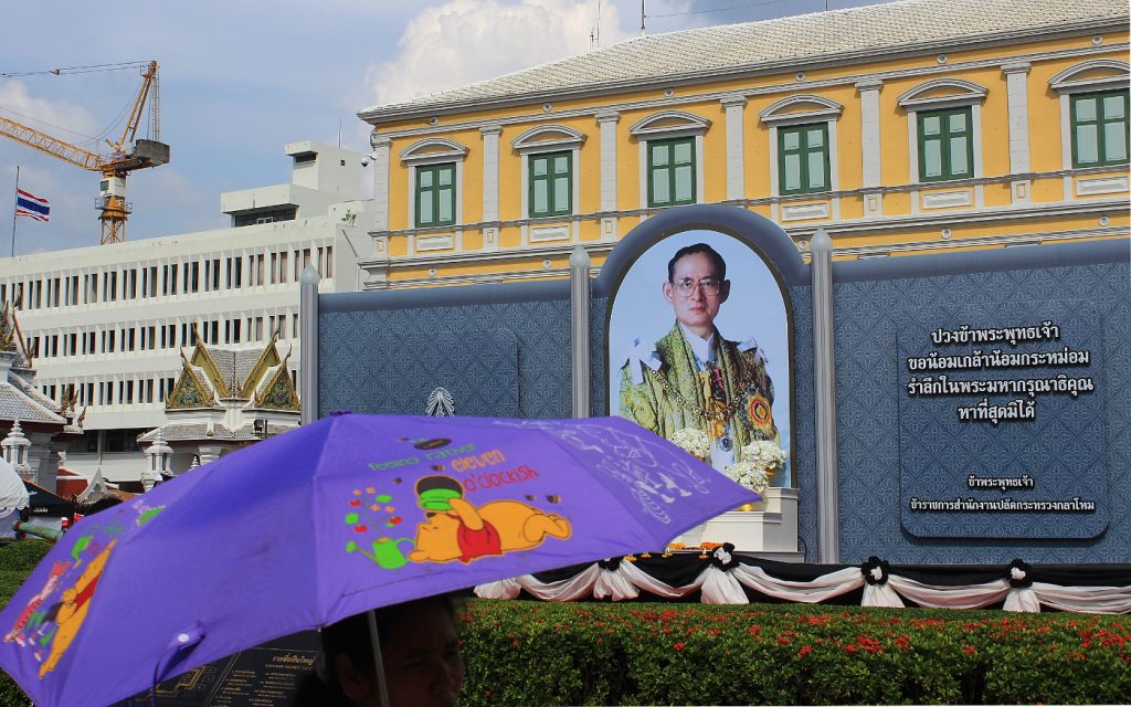 A woman holding a purple Winnie the Pooh umbrella in front of a King Bhumibol honour.
