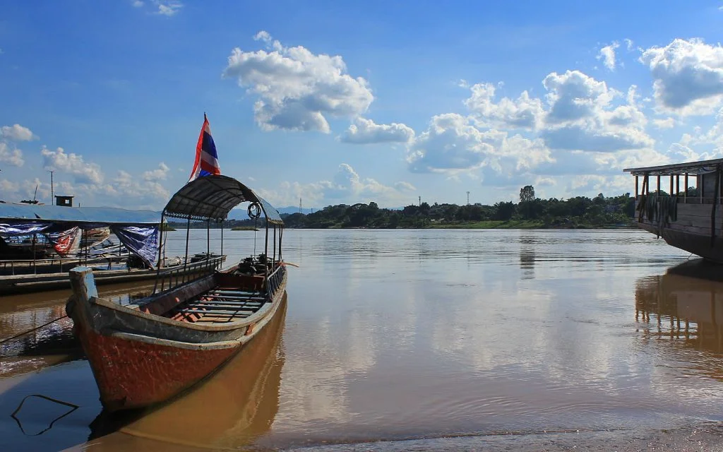 What travel teaches you about life and happiness? A slowboat on the coast of Mekong River in Huay Xai, Laos, with blue sky in the background.