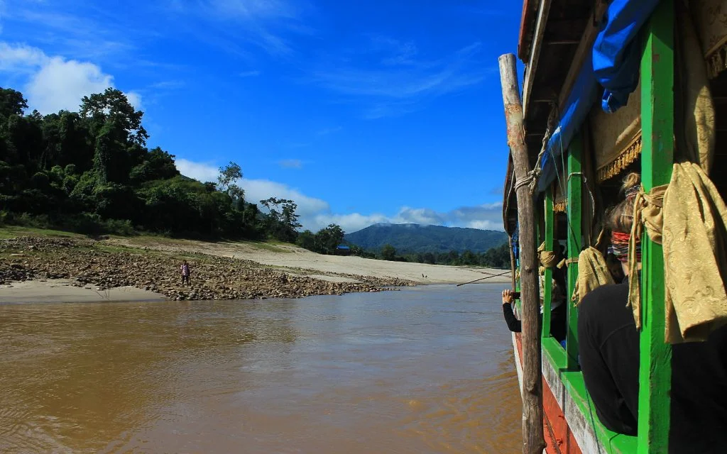 Slow boat to Luang Prabang stopping on a sandy shore with only one man visible on the coast.