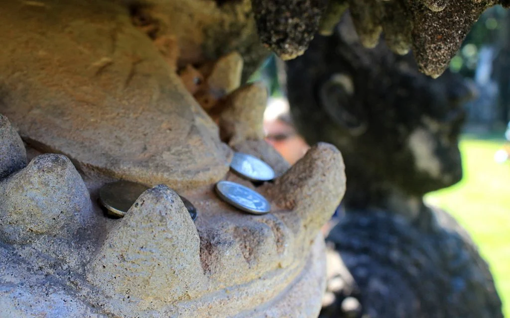 Coins inside the mouth of a crocodile statue in Buddha Park, Laos.