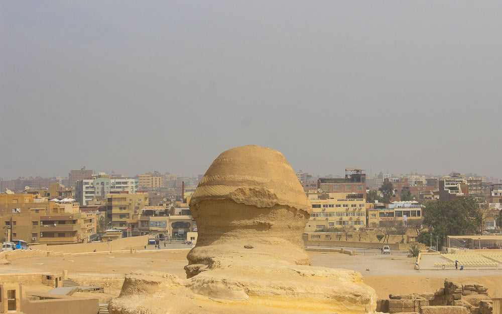 The Sphinx of Giza from behind with Cairo and smog in the background.